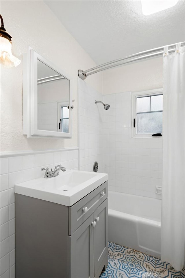 bathroom with wainscoting, tile patterned floors, shower / bath combo with shower curtain, vanity, and tile walls