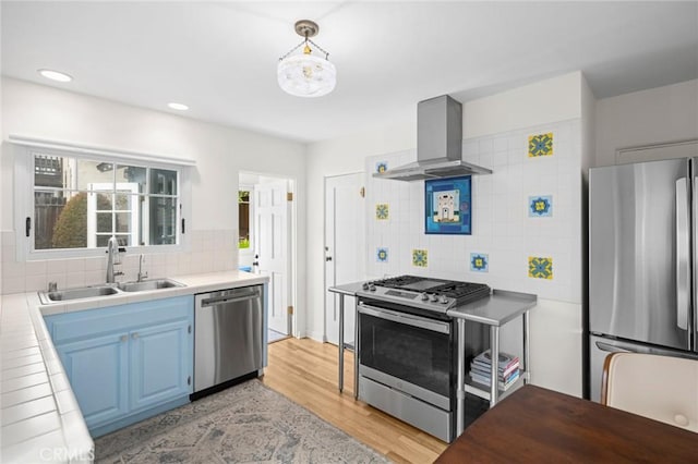 kitchen with wall chimney exhaust hood, blue cabinets, a sink, stainless steel appliances, and backsplash