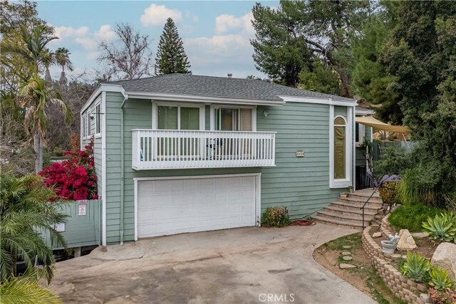 back of property with a garage, driveway, a shingled roof, and a balcony