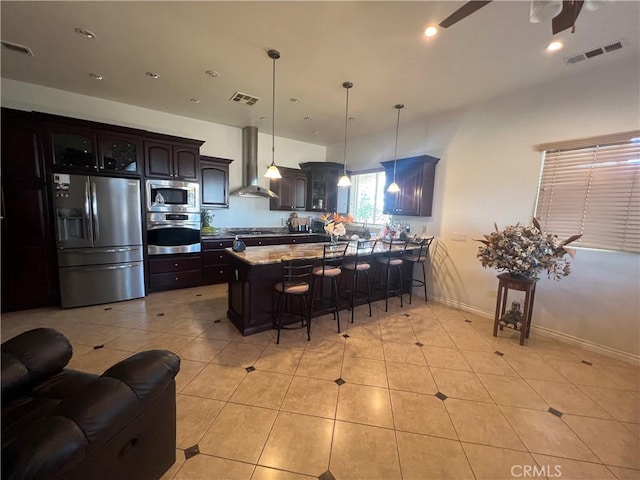 kitchen with wall chimney exhaust hood, visible vents, stainless steel appliances, and a breakfast bar area