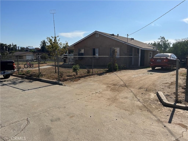 view of front of home featuring fence, dirt driveway, and stucco siding