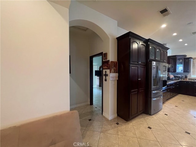 kitchen with arched walkways, recessed lighting, light tile patterned flooring, dark brown cabinets, and stainless steel fridge