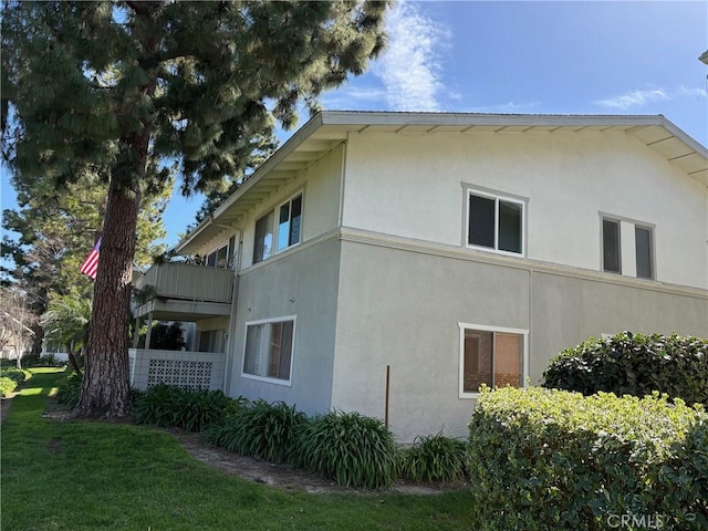 view of side of home with a yard, a balcony, and stucco siding