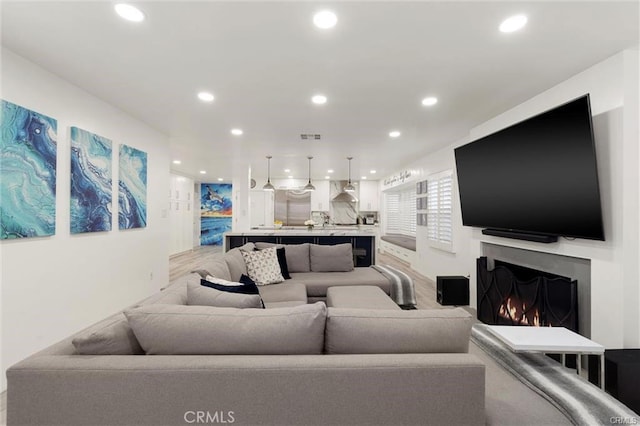 living area with a warm lit fireplace, visible vents, and recessed lighting