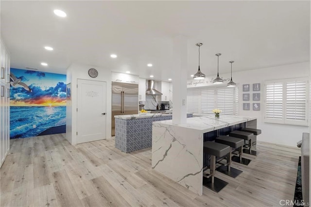 kitchen with a spacious island, light wood-type flooring, built in fridge, and wall chimney exhaust hood