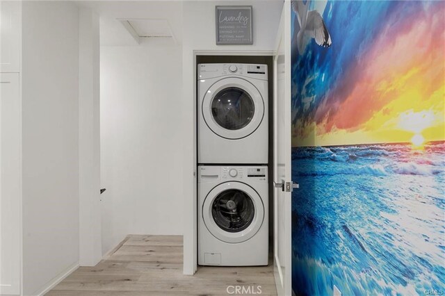 clothes washing area with stacked washer and dryer, attic access, laundry area, and wood finished floors