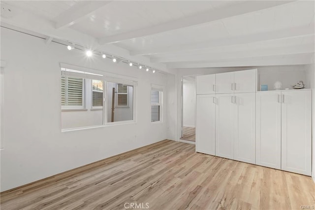 unfurnished room featuring light wood finished floors, rail lighting, and beam ceiling