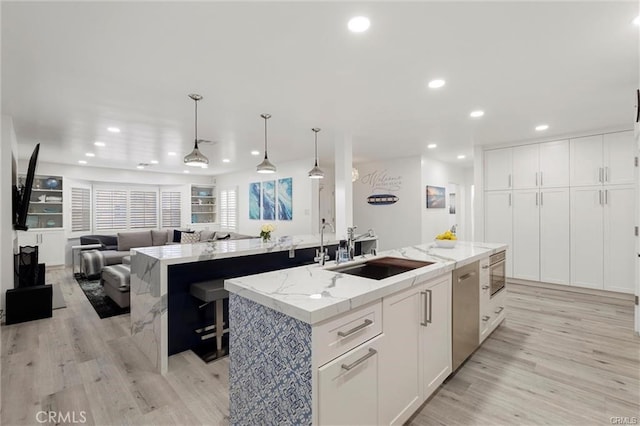 kitchen featuring a center island with sink, light wood-style floors, open floor plan, white cabinets, and a sink