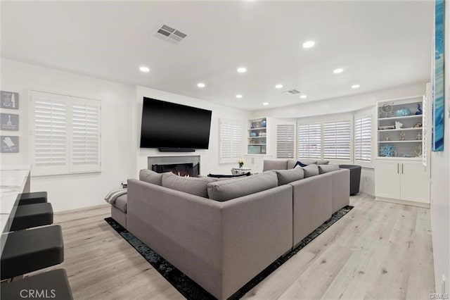 living area featuring light wood-type flooring, a warm lit fireplace, visible vents, and recessed lighting