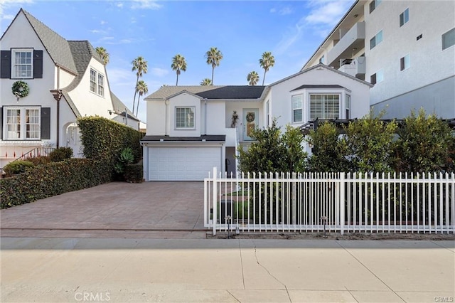 english style home with a garage, driveway, fence, and stucco siding