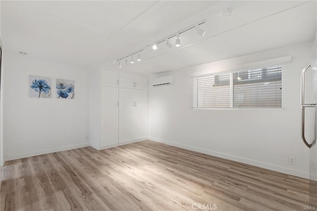 unfurnished room with light wood finished floors, a wall mounted air conditioner, and baseboards