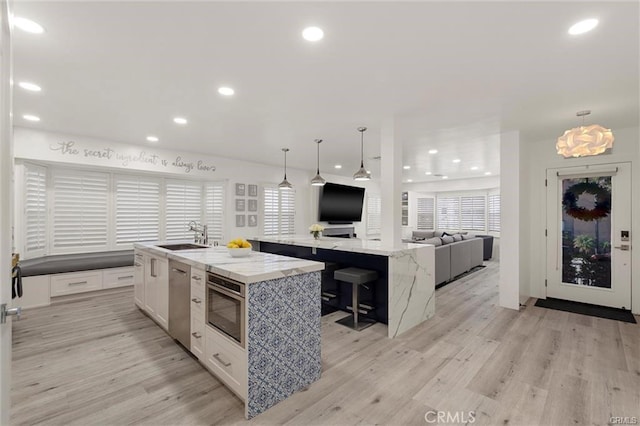 kitchen with a large island, stainless steel appliances, white cabinets, a sink, and light wood-type flooring