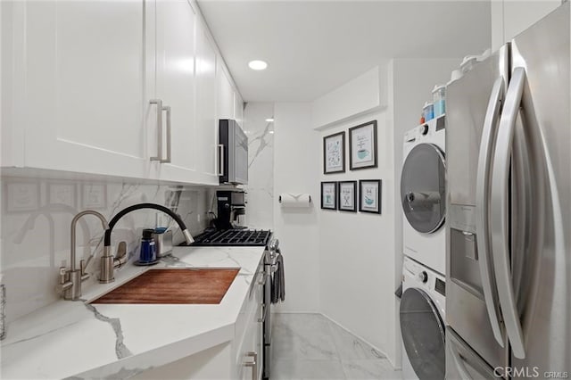 laundry room featuring stacked washer and clothes dryer, marble finish floor, recessed lighting, a sink, and laundry area