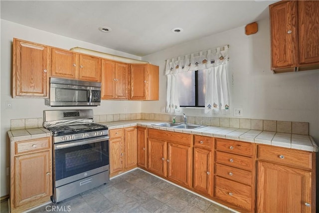 kitchen with stainless steel appliances, brown cabinets, a sink, and tile countertops