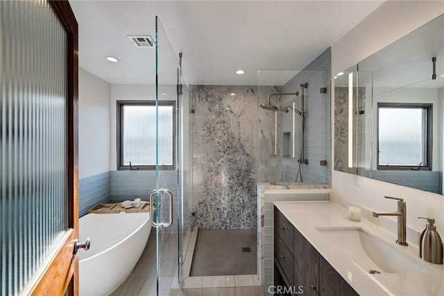 full bath with visible vents, vanity, tile walls, a soaking tub, and a stall shower