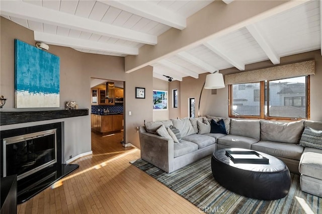 living room featuring a wealth of natural light, a glass covered fireplace, wood-type flooring, and vaulted ceiling with beams