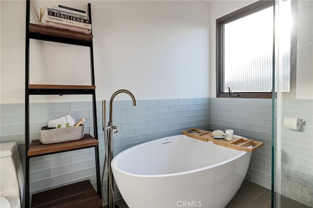 bathroom with a wainscoted wall, a soaking tub, and tile walls