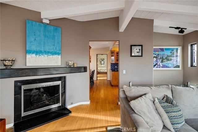 living area with lofted ceiling with beams, wood finished floors, and a glass covered fireplace