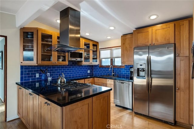 kitchen featuring light wood finished floors, appliances with stainless steel finishes, a sink, island range hood, and a peninsula