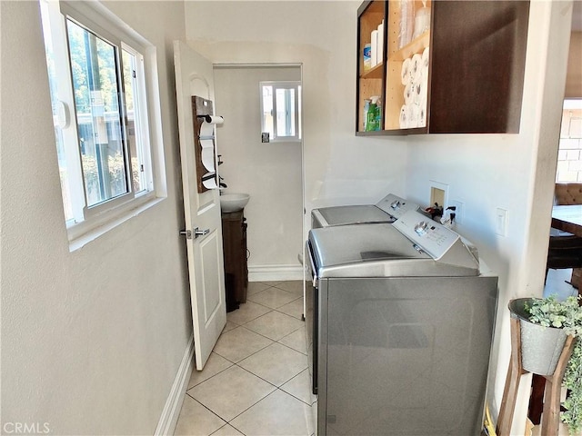 laundry area featuring light tile patterned floors, separate washer and dryer, cabinet space, and baseboards