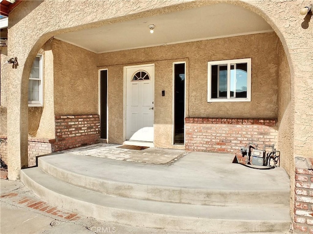 view of exterior entry with brick siding and stucco siding