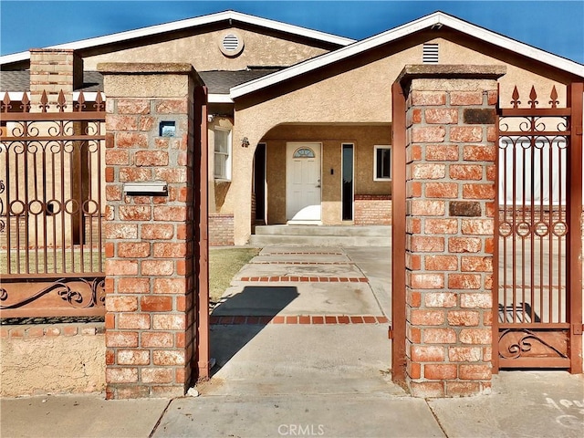 view of exterior entry featuring a gate, brick siding, fence, and stucco siding