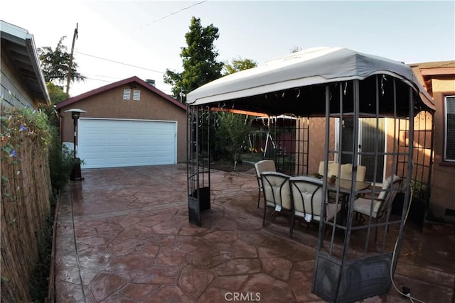 view of patio featuring a garage, outdoor dining space, an outdoor structure, and fence