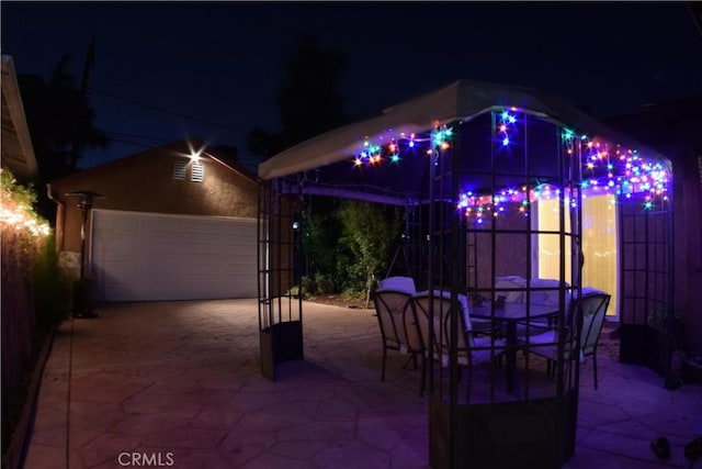 patio at twilight with a garage, an outbuilding, and outdoor dining space