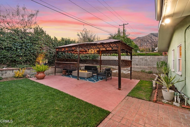 patio terrace at dusk featuring an outdoor fire pit, a gazebo, a lawn, a fenced backyard, and a mountain view