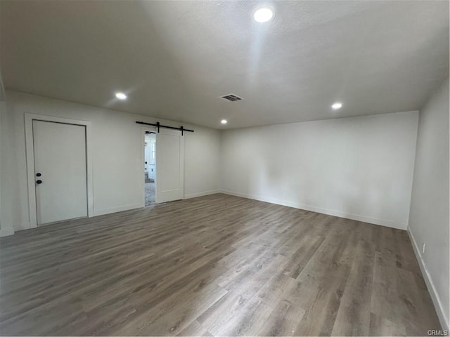 unfurnished room featuring a barn door, recessed lighting, wood finished floors, and baseboards