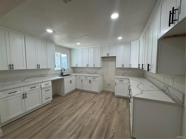 kitchen with light stone countertops, light wood-type flooring, white cabinetry, a sink, and recessed lighting