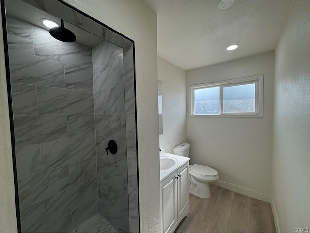 bathroom with toilet, a stall shower, vanity, wood finished floors, and baseboards