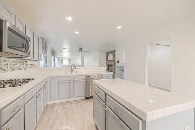 kitchen with stainless steel appliances, a sink, backsplash, tile counters, and light wood finished floors