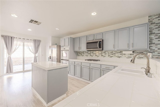 kitchen featuring tile counters, visible vents, stainless steel appliances, gray cabinetry, and a sink