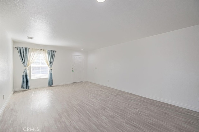 spare room featuring light wood finished floors, baseboards, visible vents, and a textured ceiling