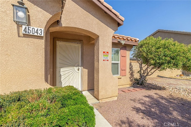 doorway to property featuring a tiled roof, fence, and stucco siding