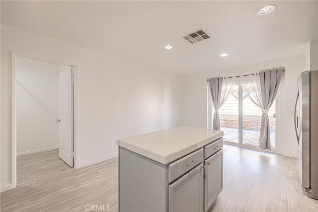 kitchen with tile countertops, gray cabinetry, visible vents, freestanding refrigerator, and light wood finished floors