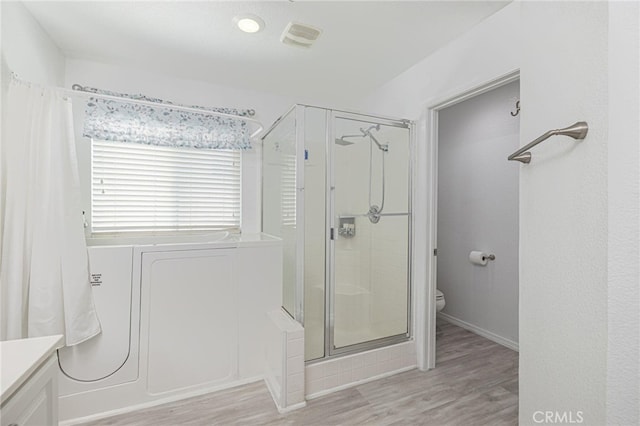 full bathroom featuring toilet, a bathing tub, a stall shower, vanity, and wood finished floors