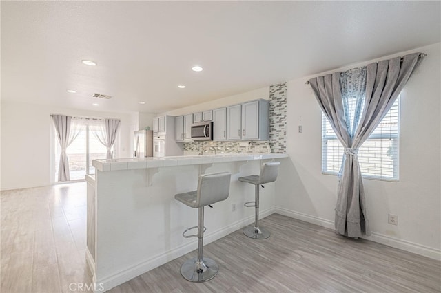 kitchen featuring stainless steel appliances, gray cabinetry, tile countertops, and a kitchen bar