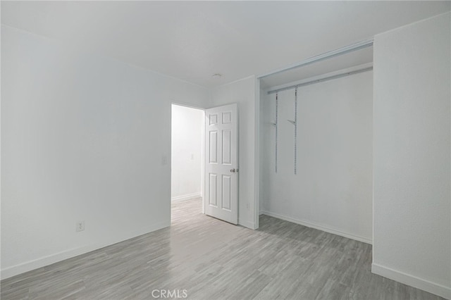 unfurnished bedroom featuring light wood-type flooring, a closet, and baseboards