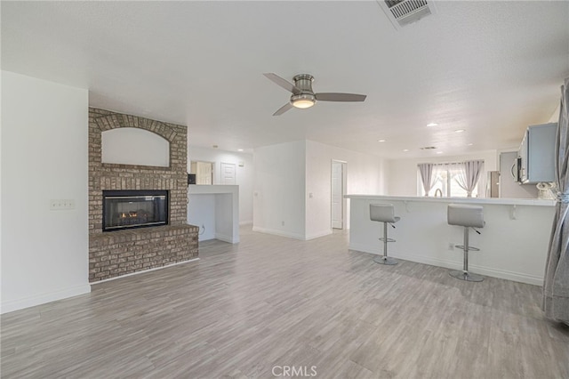 unfurnished living room featuring ceiling fan, a fireplace, visible vents, baseboards, and light wood-type flooring