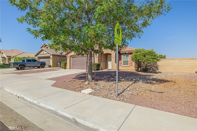 view of front of home featuring an attached garage, fence, a tile roof, driveway, and stucco siding