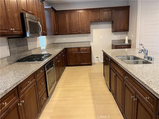 kitchen featuring dark brown cabinetry, appliances with stainless steel finishes, light stone counters, and a sink