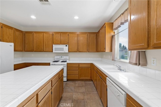 kitchen with tile counters, white appliances, visible vents, and a sink