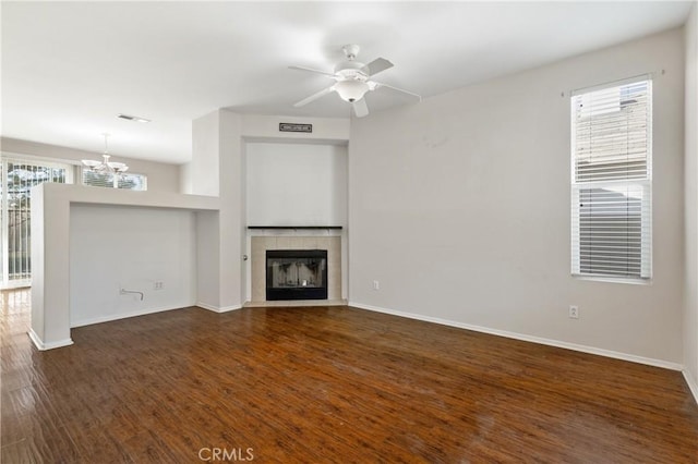 unfurnished living room featuring baseboards, visible vents, a tiled fireplace, dark wood-style flooring, and ceiling fan with notable chandelier