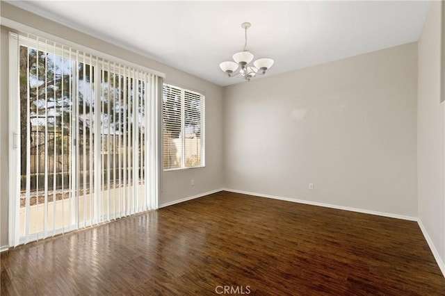 spare room with a chandelier, dark wood finished floors, and baseboards