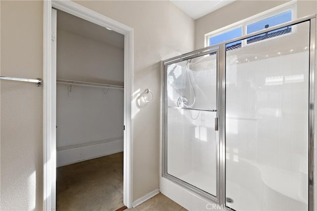 bathroom with a stall shower, a spacious closet, and baseboards