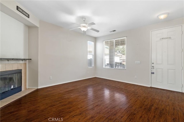 unfurnished living room with a tile fireplace, visible vents, baseboards, and wood finished floors