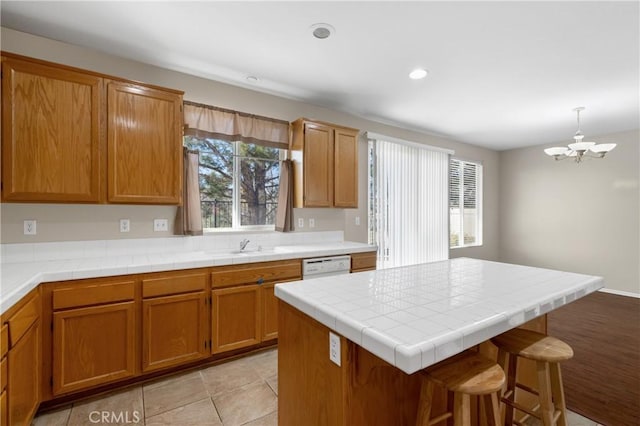 kitchen with brown cabinetry, a breakfast bar, dishwasher, and a sink