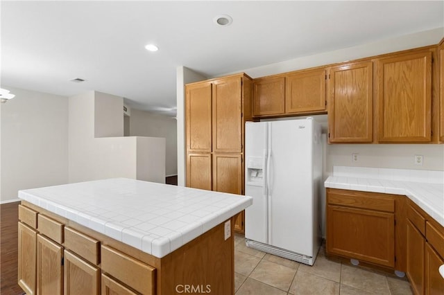 kitchen with white fridge with ice dispenser, brown cabinets, a kitchen island, and recessed lighting